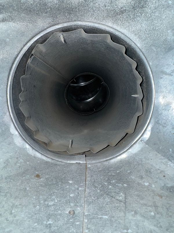 Metal duct opening with jagged edges and a dark interior.