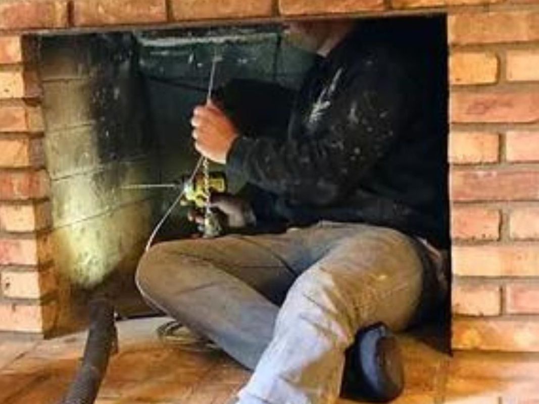Person cleans a brick fireplace, using a tool.