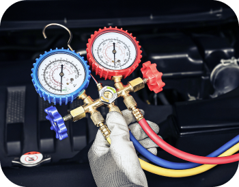 A person is holding a set of gauges and hoses in front of a car engine. | NRH Automotive