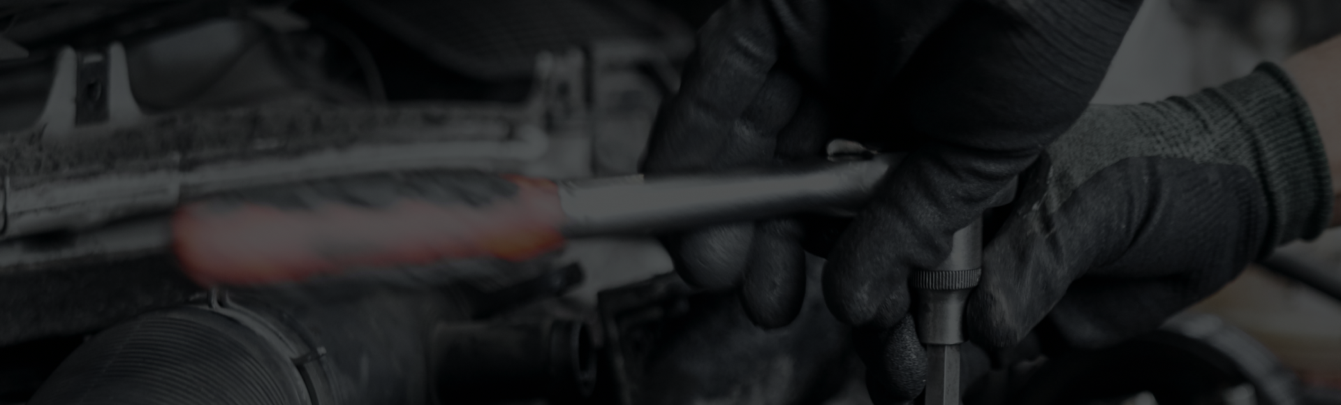 A man wearing black gloves is working on a car engine with a wrench. | NRH Automotive