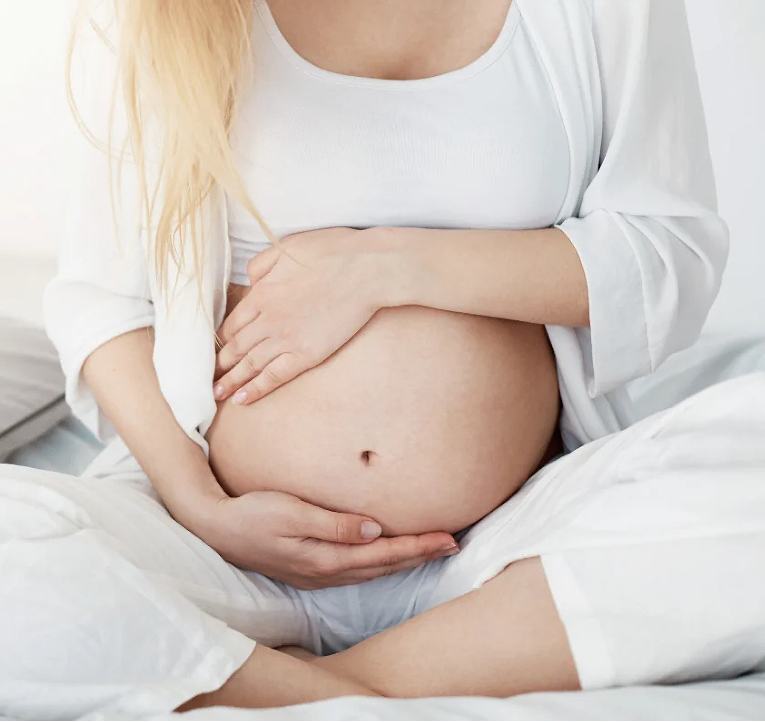 Mulher grávida vestida de branco segurando sua barriga.