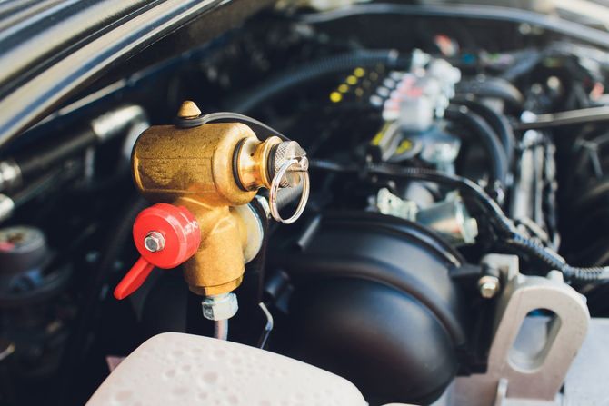 Valvola in ottone con maniglia rossa nel vano motore di un'auto.