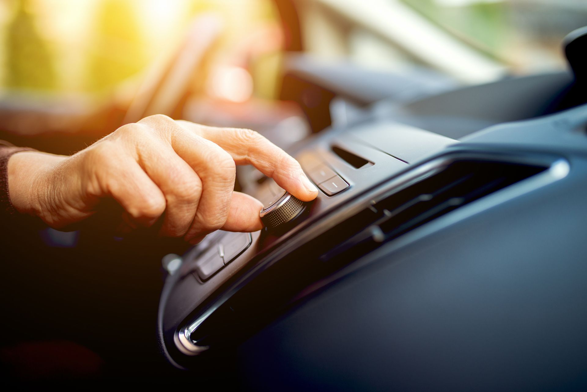 Mano che gira una manopola sul cruscotto di un'auto, probabilmente per regolare i comandi della radio o del climatizzatore.