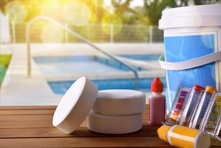 Poolside swim gear with sunscreen, pills, and a cooler on a wooden table