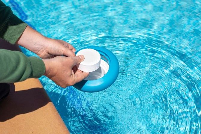 Hands placing a white pool cleaner over blue pool water