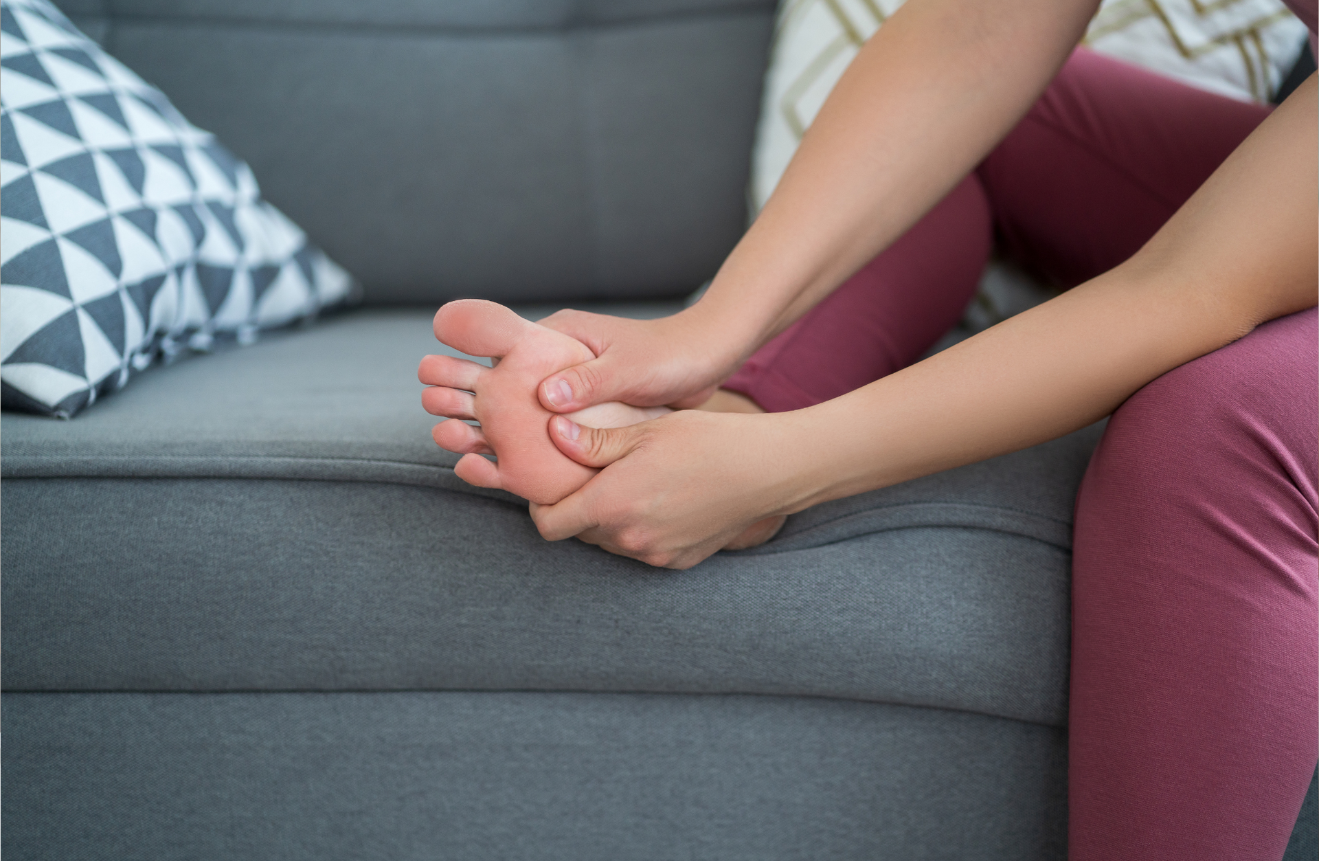 Toetal footcare Podiatrists, Cardiff & Pontypridd A woman is sitting on a couch holding her foot in pain.