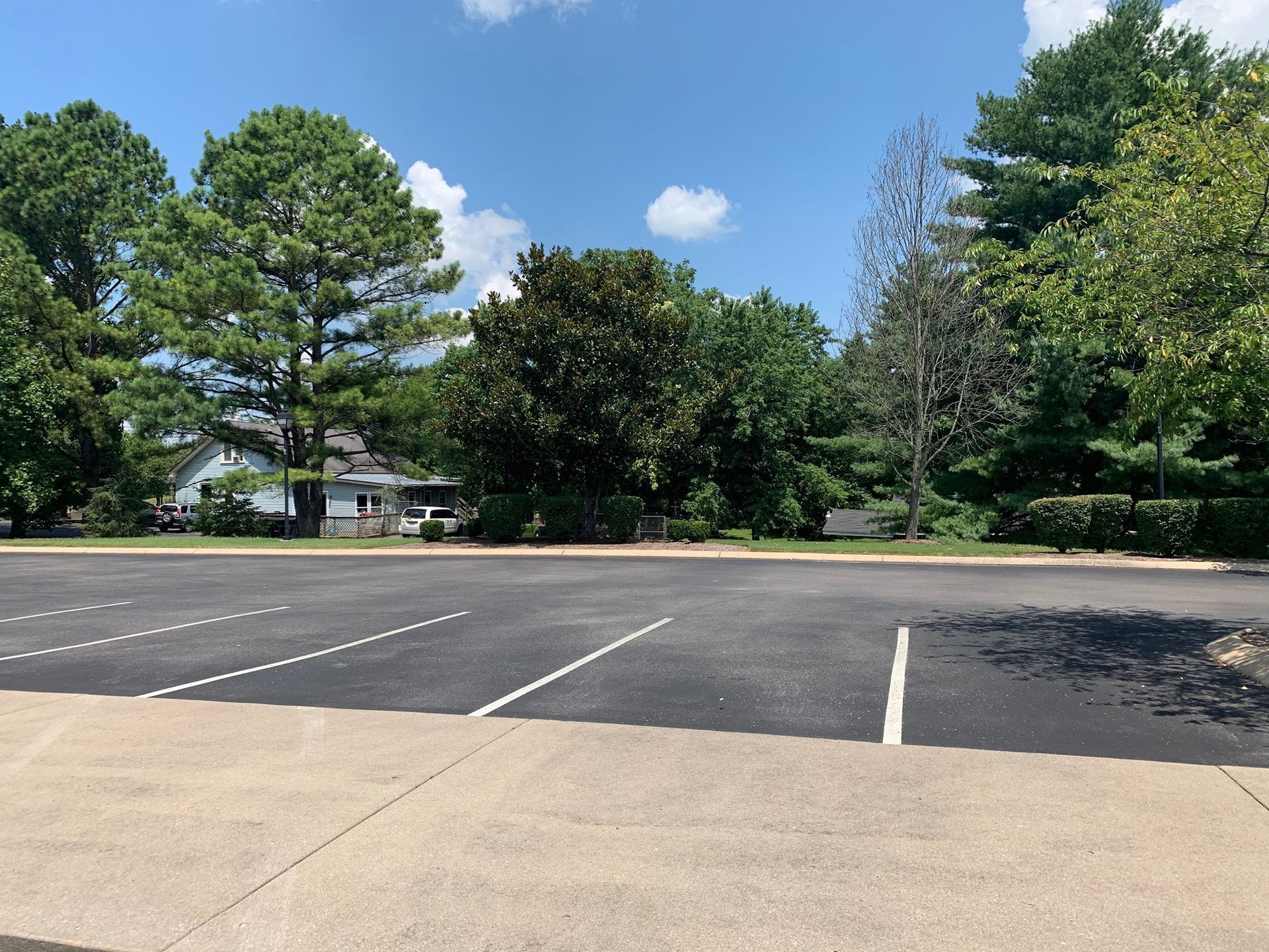 A parking lot with trees and a house in the background