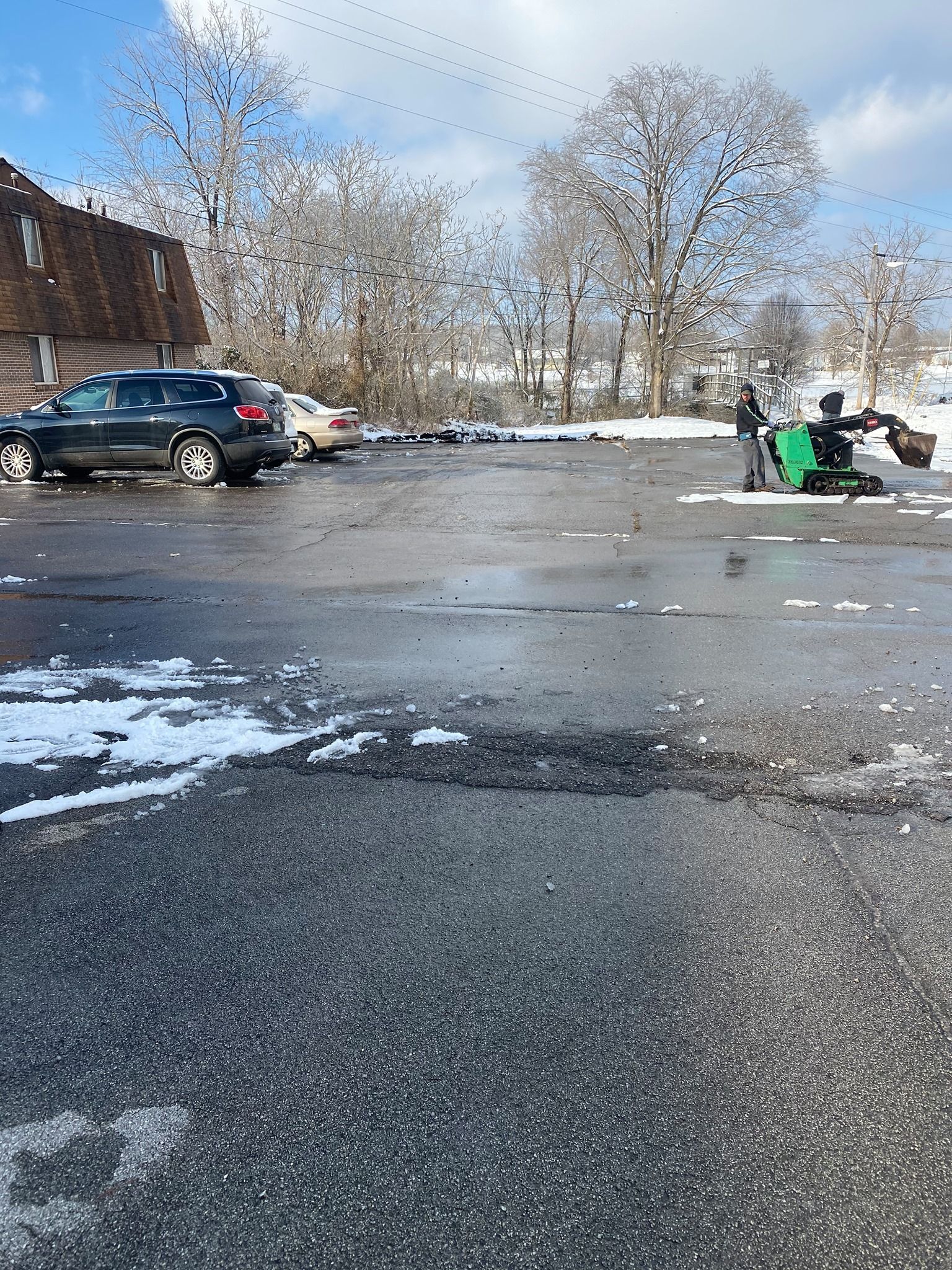 A man is using a lawn mower to remove snow from a parking lot.