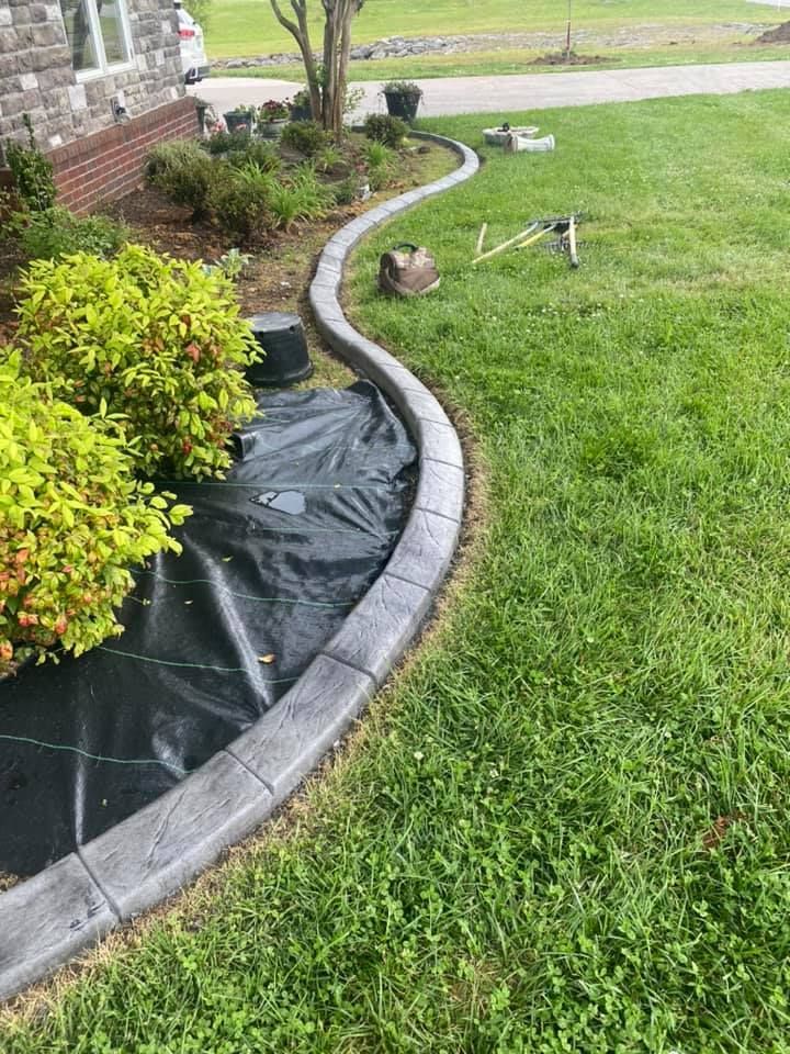 A concrete curb is being installed on the side of a lush green lawn.