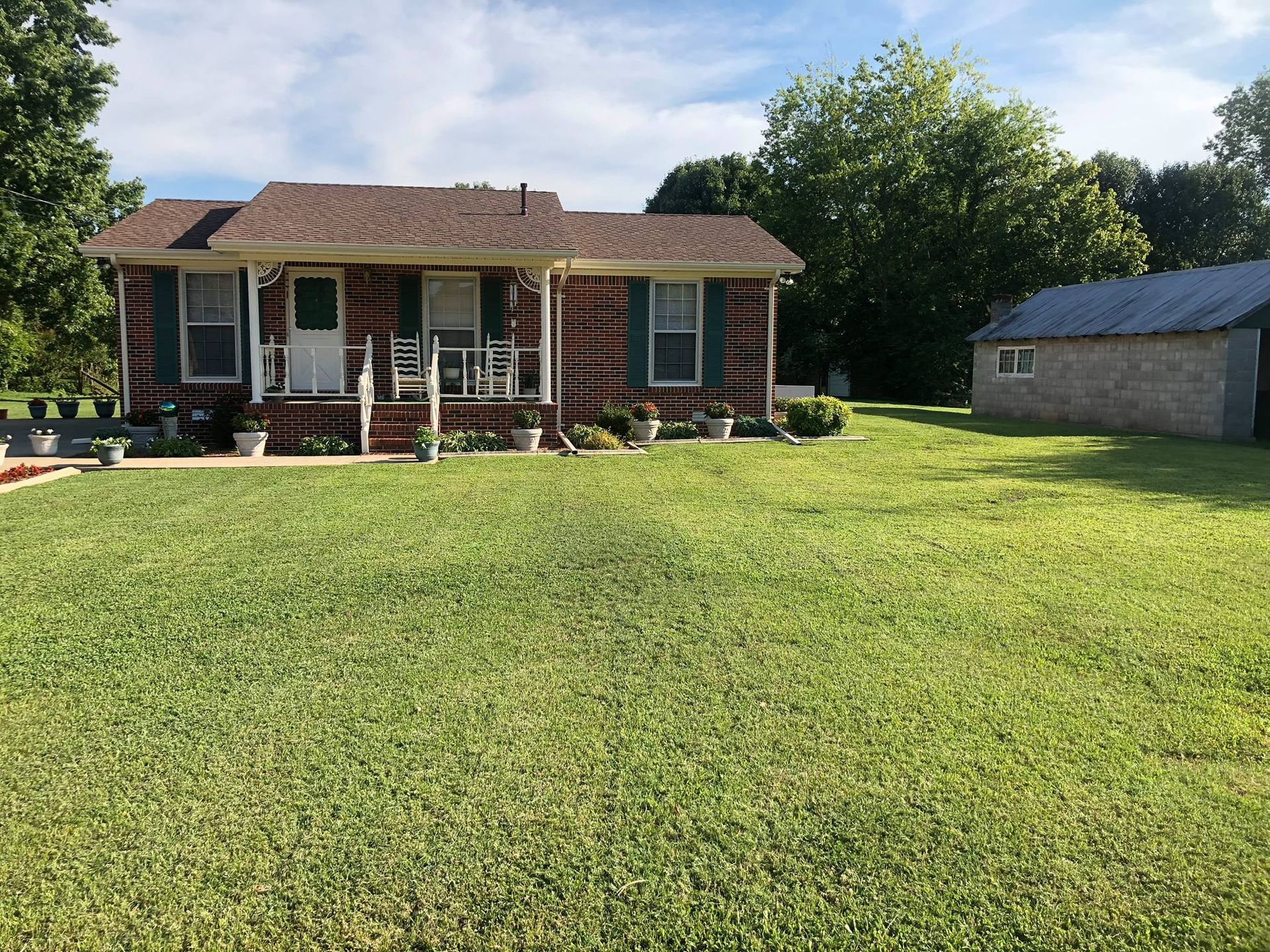 A brick house with a porch and a large lawn in front of it.