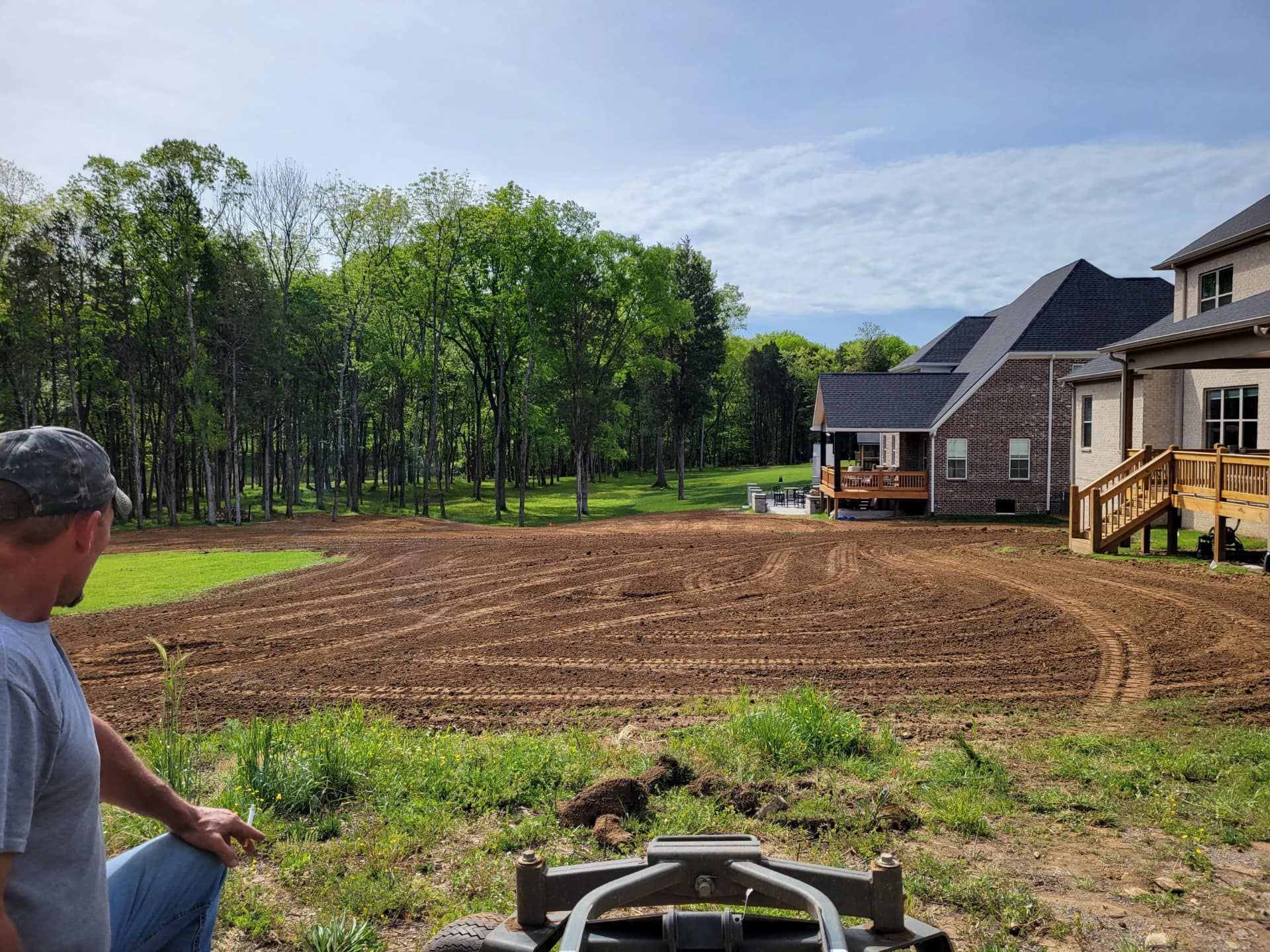 A man is standing in a dirt field in front of a house.