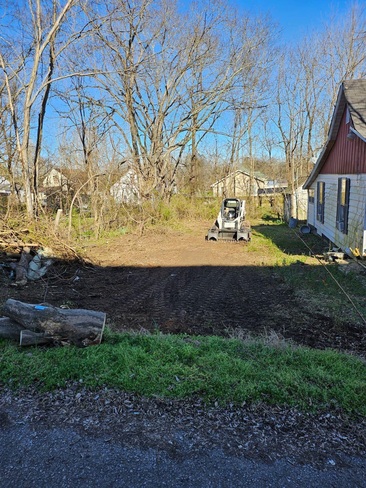 A bobcat is driving down a dirt road in front of a house.