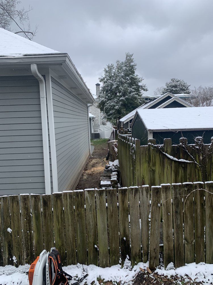 A snowy yard with a wooden fence and a house in the background.