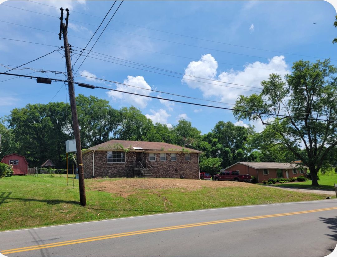 A house is sitting in the middle of a grassy field next to a road.