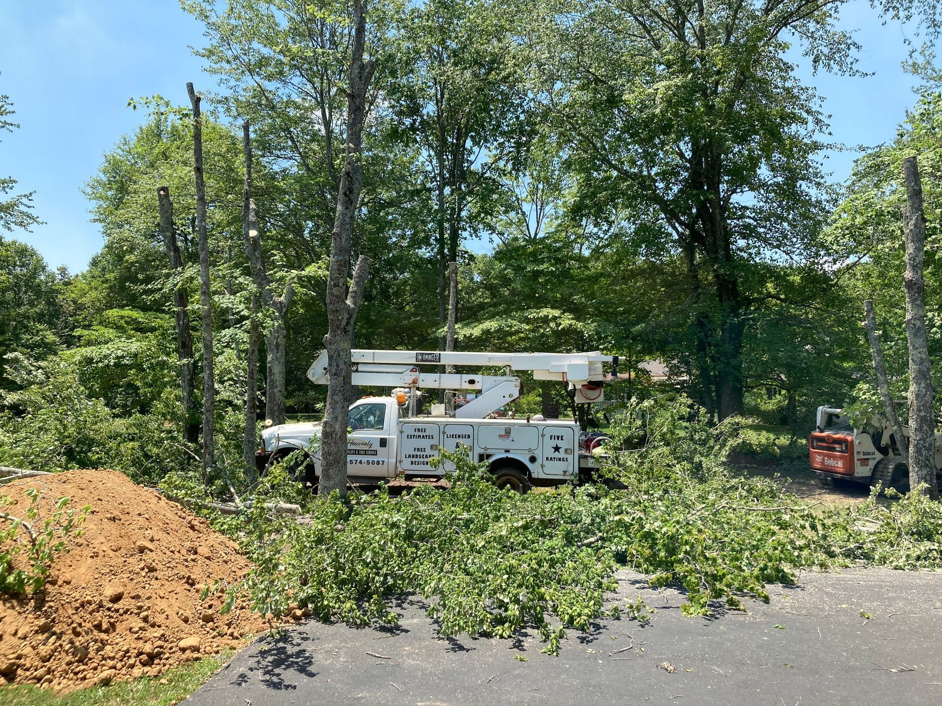 A white truck with a crane on top of it is cutting down trees.