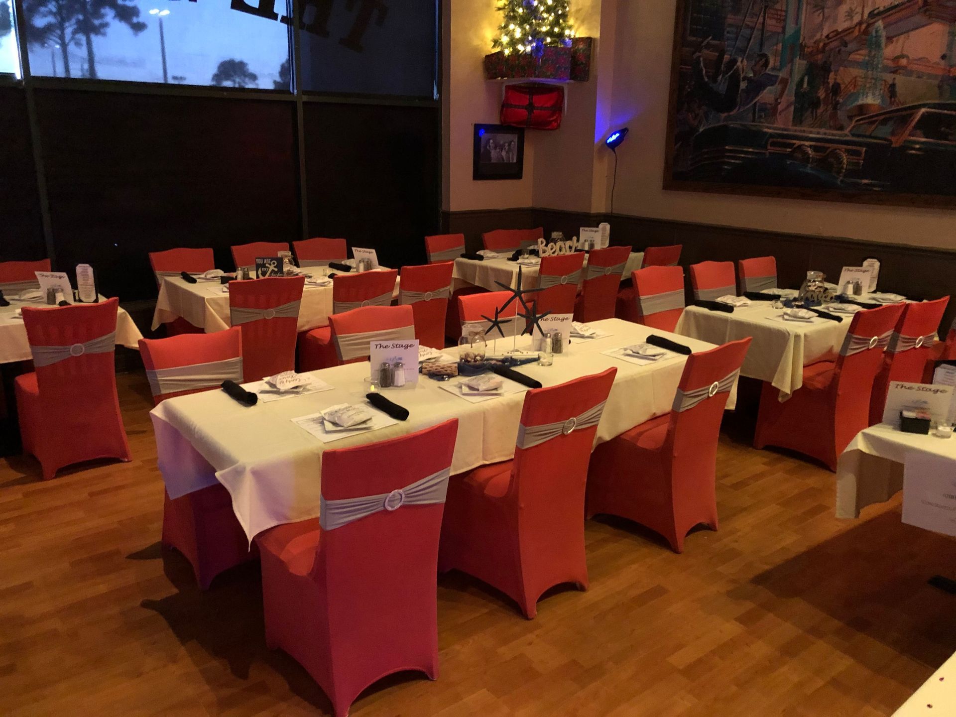 Restaurant dining room set with tables covered in white linens, red chair covers.