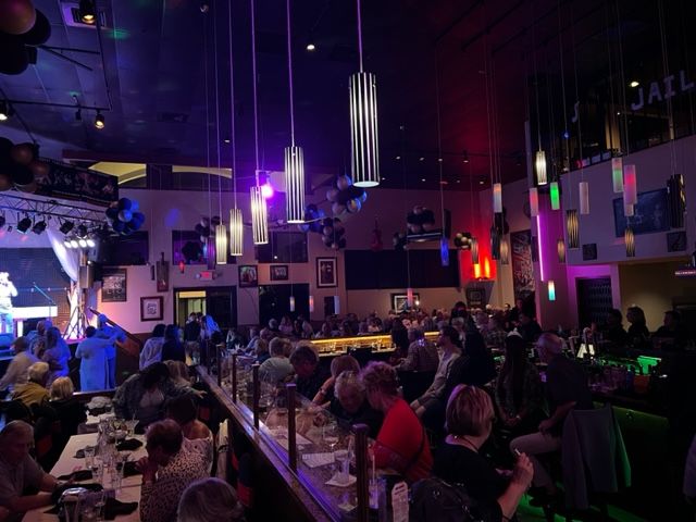 A crowd of people are sitting at tables in a restaurant with purple lights hanging from the ceiling