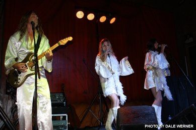 A man is playing a guitar and two women are singing on stage.