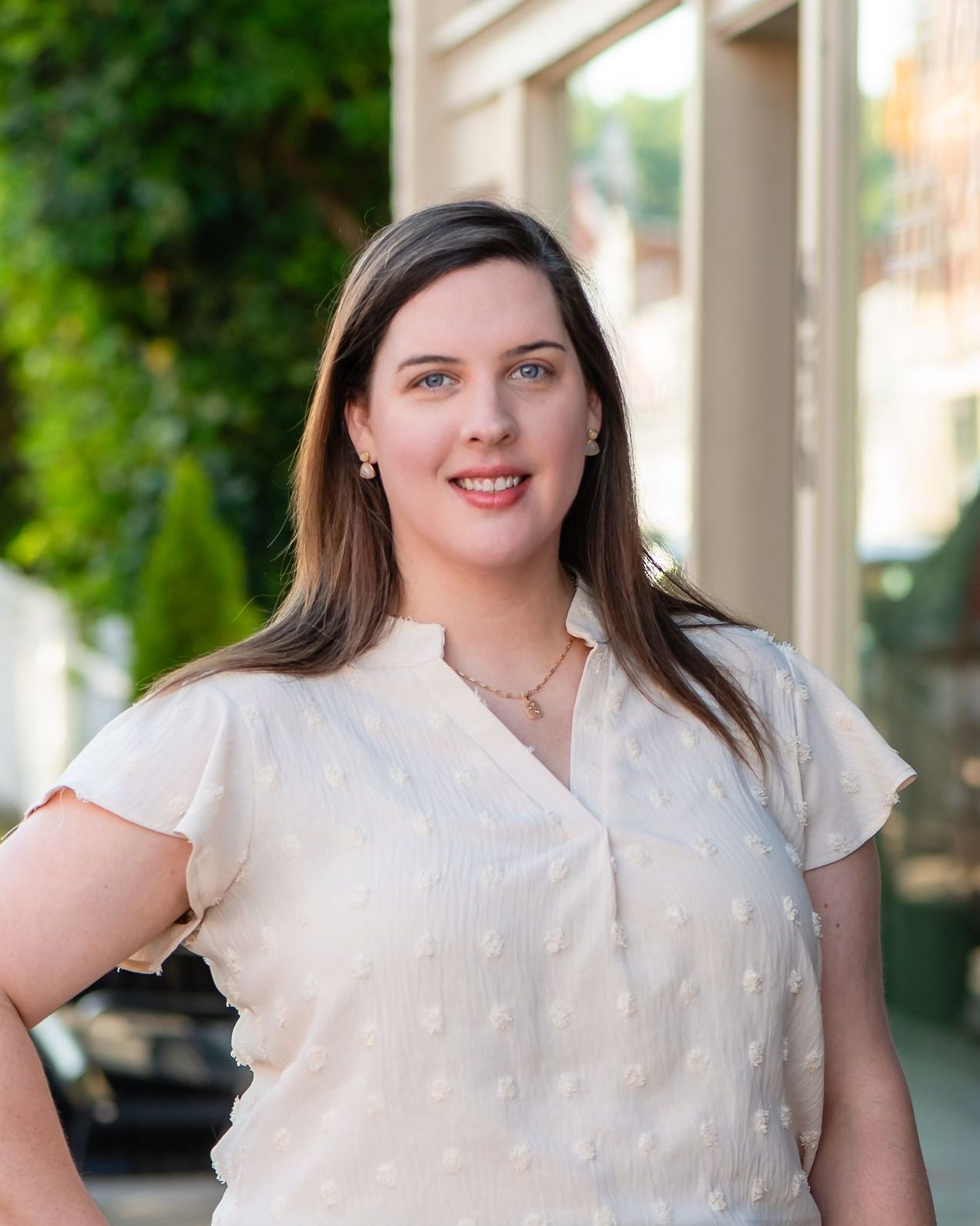 A woman in a white shirt is standing in front of a building.