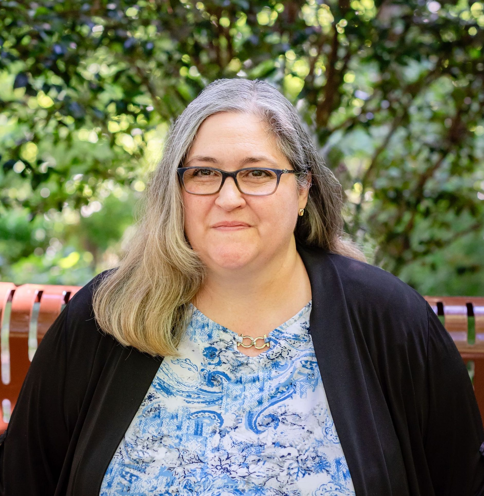 A woman wearing glasses and a blue shirt is sitting on a bench.