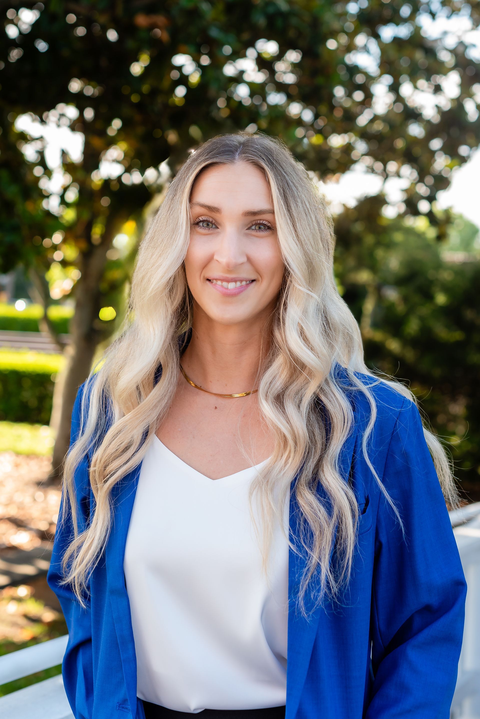 A woman wearing a blue jacket and a white shirt is sitting on a bench.