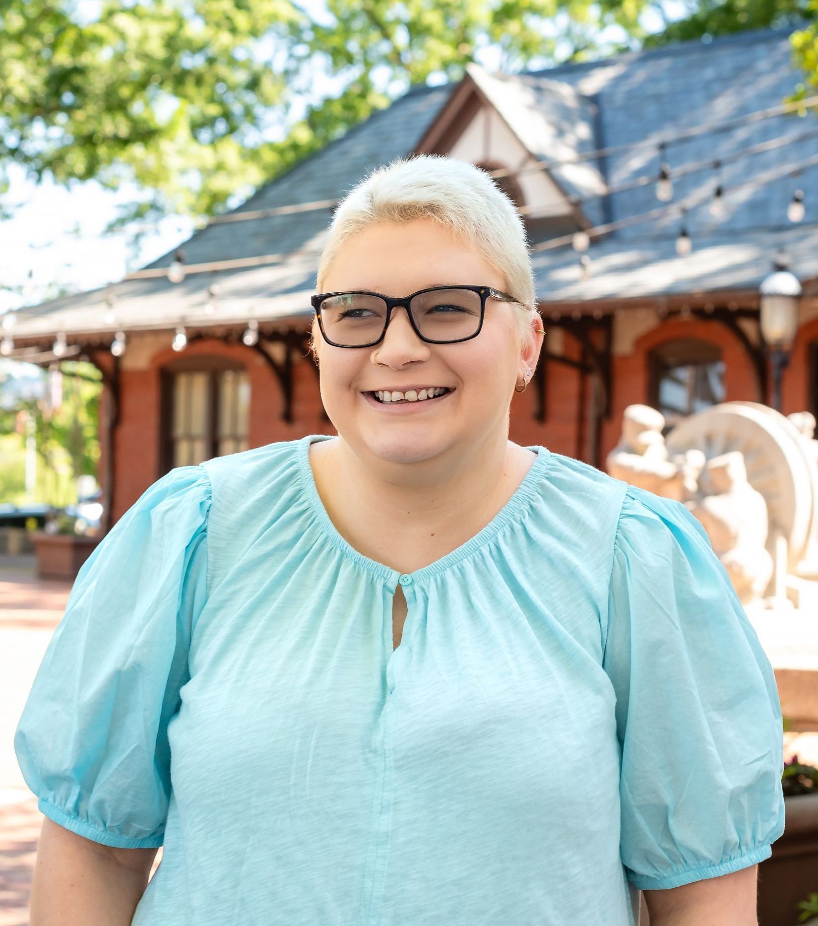 A woman in a white shirt is standing in front of a building.