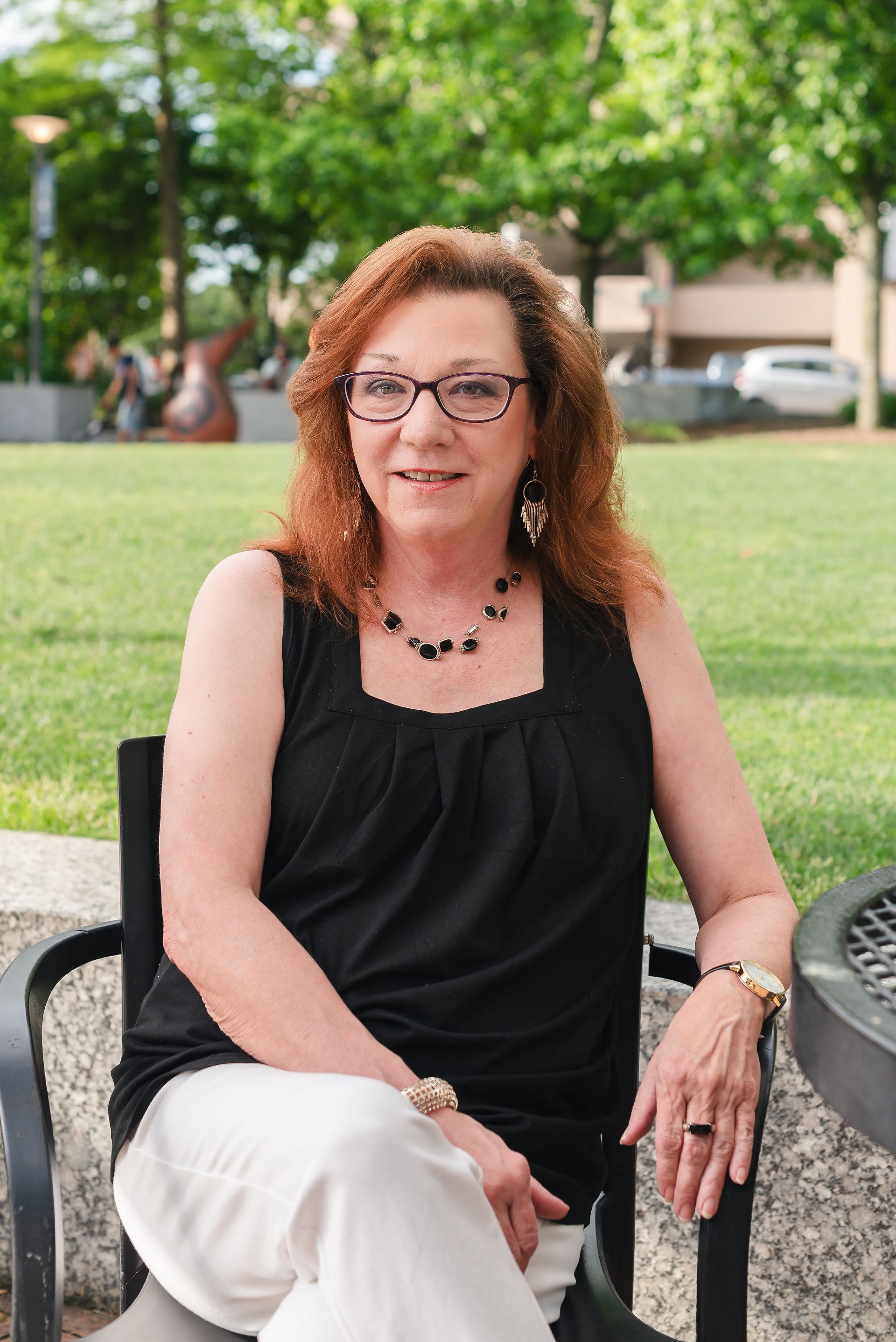 A woman wearing glasses is sitting on a bench in a park.