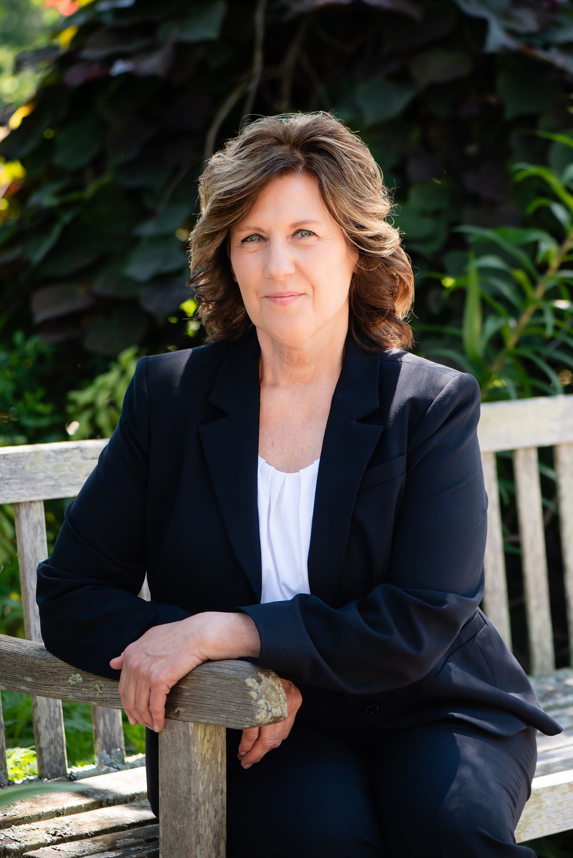 A woman in a black jacket is sitting on a wooden bench.