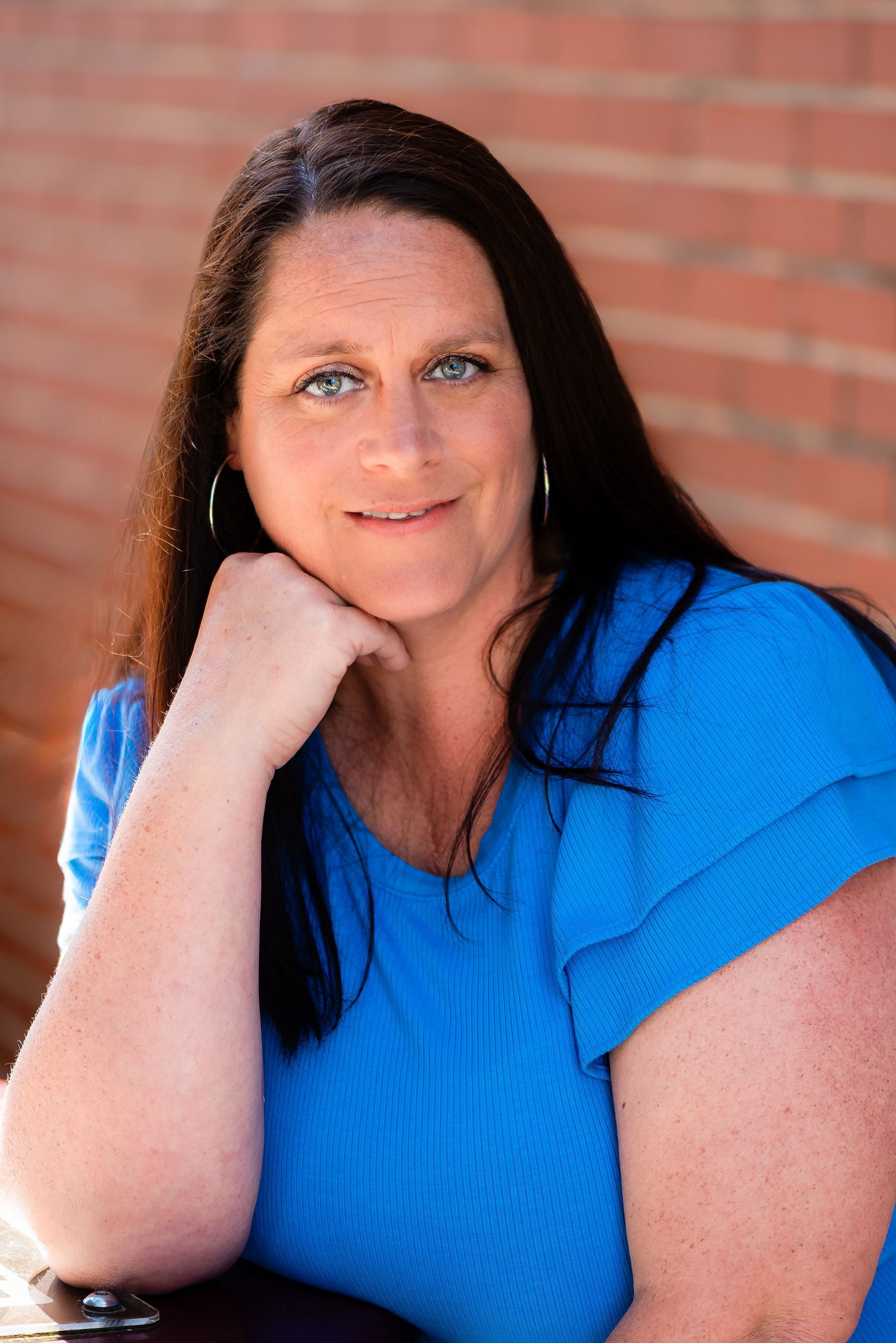 A woman in a blue shirt is sitting in front of a brick wall.