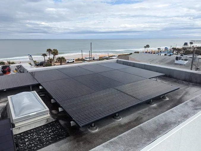 Rooftop solar panels overlook the beach and ocean on a cloudy day.
