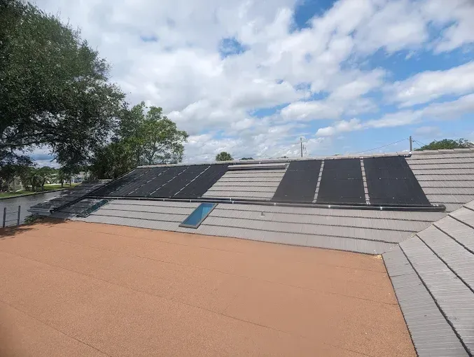 Solar panels on a tiled roof under a partly cloudy blue sky.