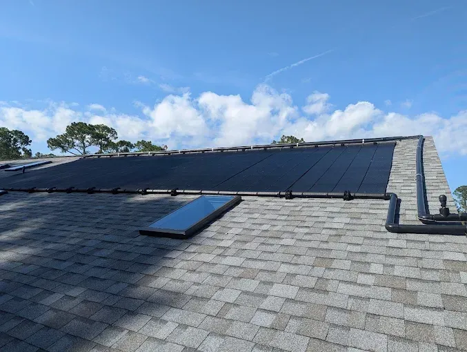 Solar panels on a shingled roof with a skylight; blue sky in the background.