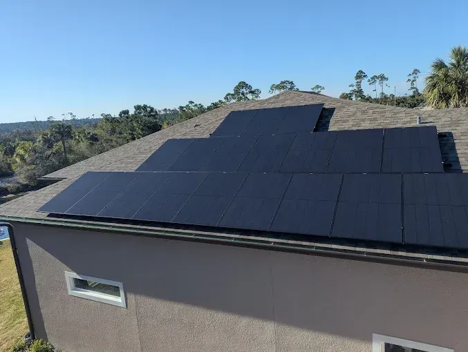 Solar panels installed on a residential roof, with a clear blue sky and trees in the background.