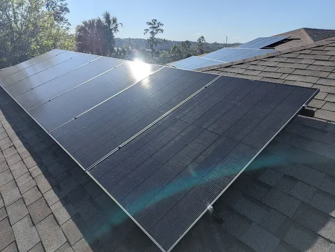 Solar panels on a shingled roof, catching the sun's reflection.