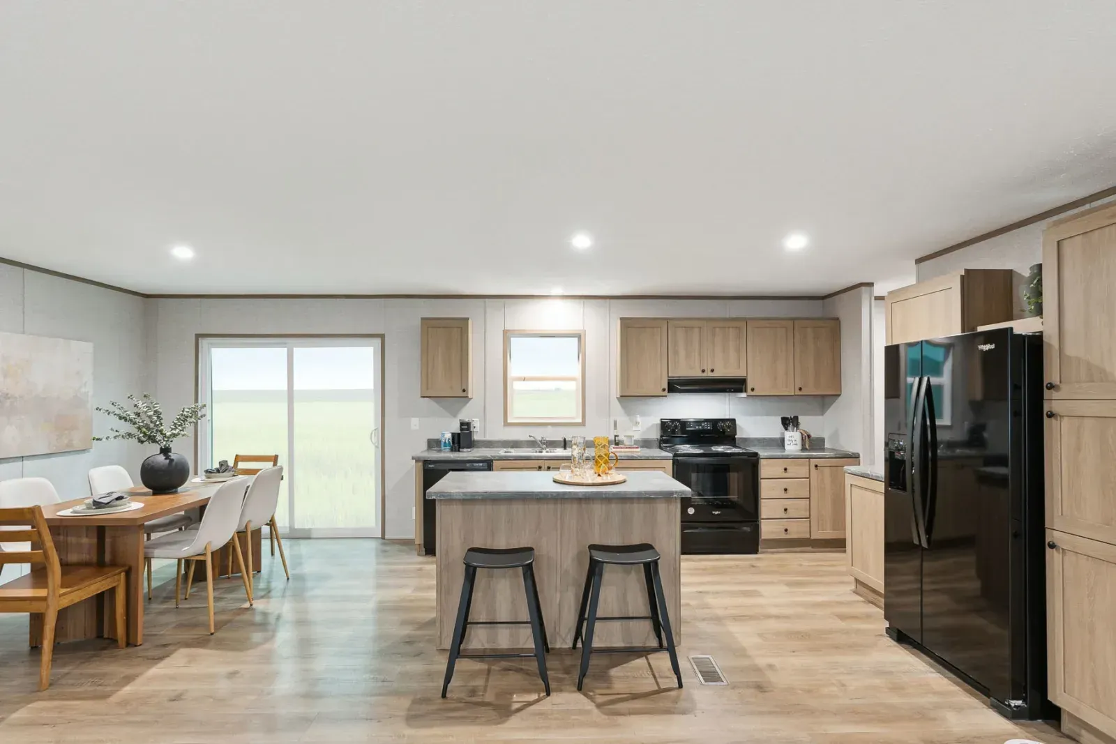 Modern kitchen and dining room with wooden cabinets, black appliances, and island.
