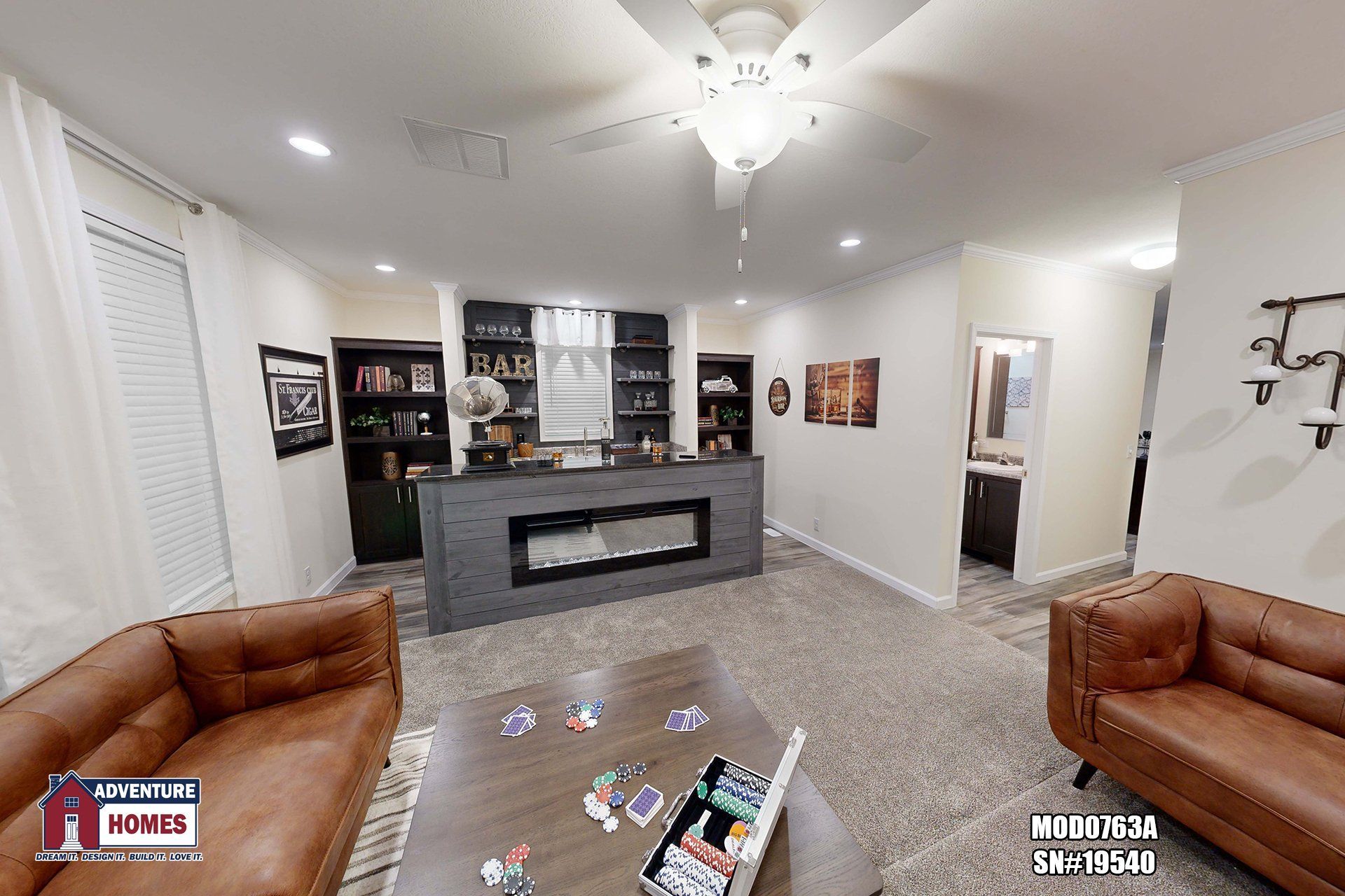 Living room with brown leather sofas, a bar with a fireplace, and a ceiling fan.