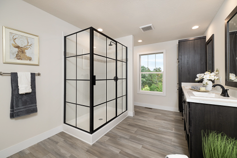 Modern bathroom with black-framed shower, dark vanity, wood-look floor, window, and artwork.