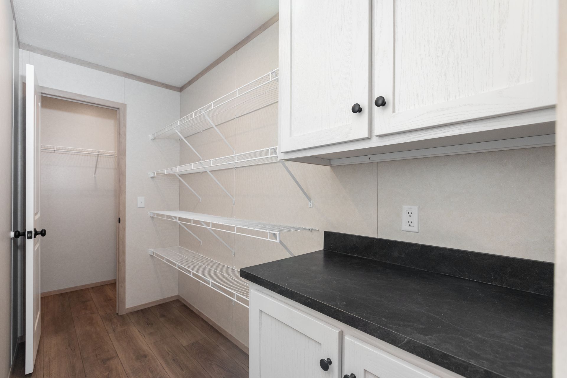Pantry with wire shelves and white cabinets with black countertop.