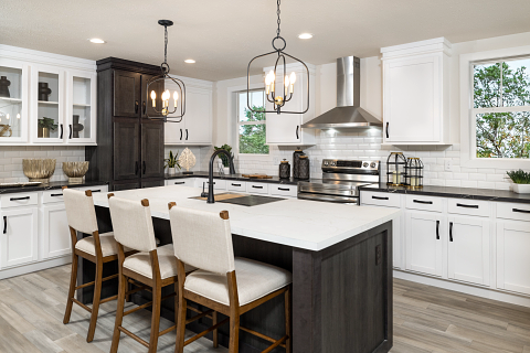 Modern kitchen with white cabinets, dark island, stainless steel appliances, and pendant lights.