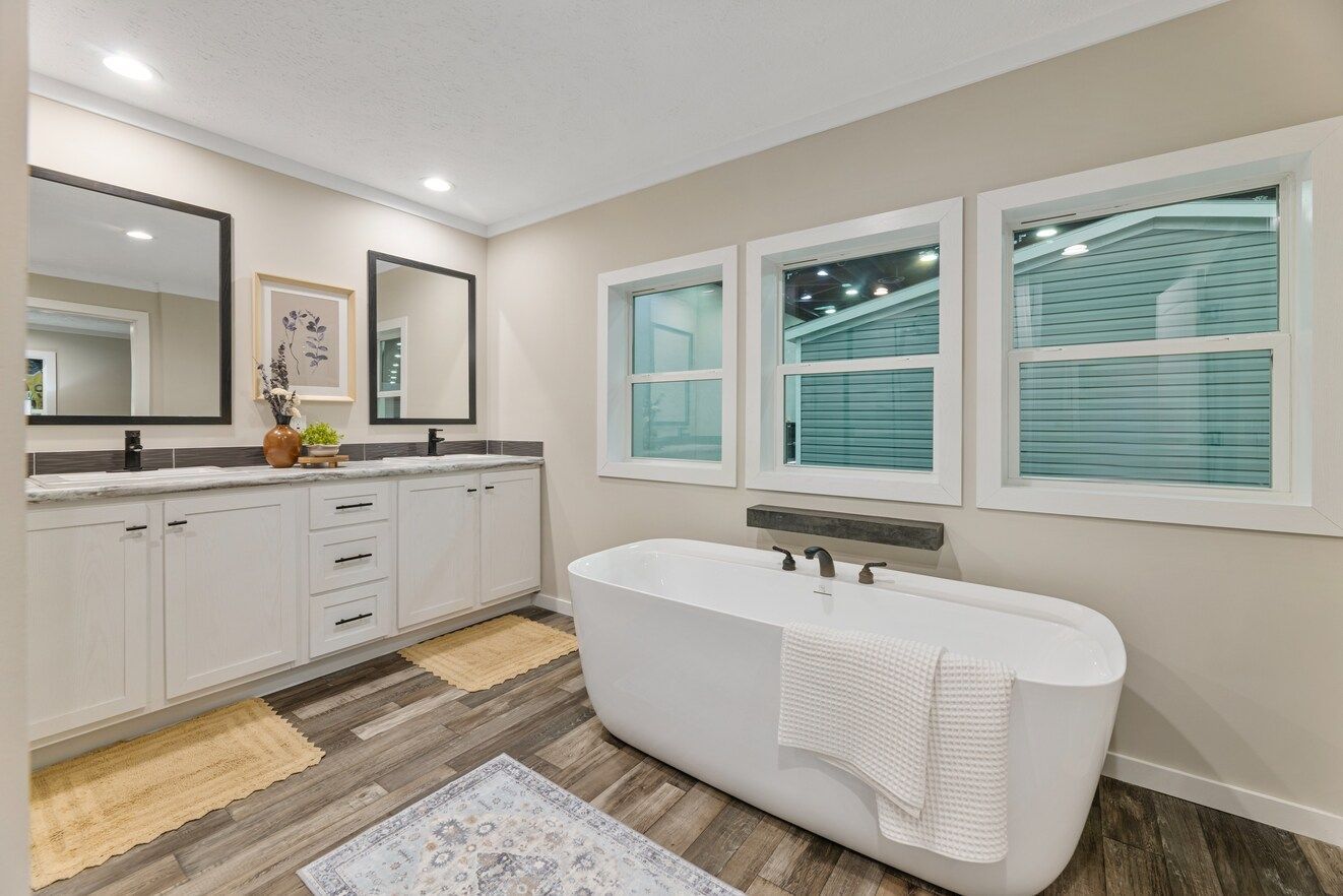 Bathroom with white tub, double vanity, and windows, featuring neutral colors and modern design.