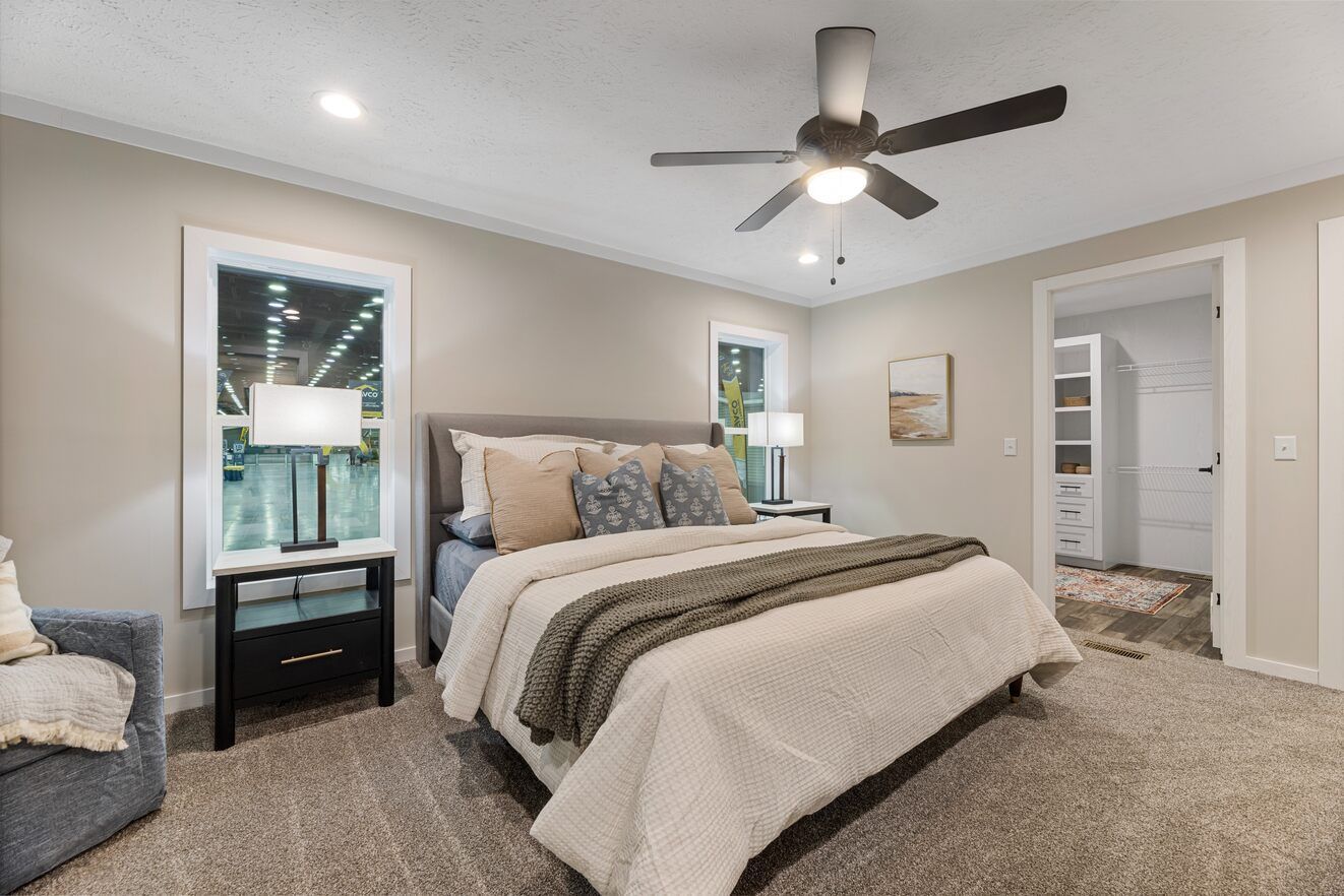 Bedroom with bed, nightstands, windows, ceiling fan, and access to a walk-in closet.