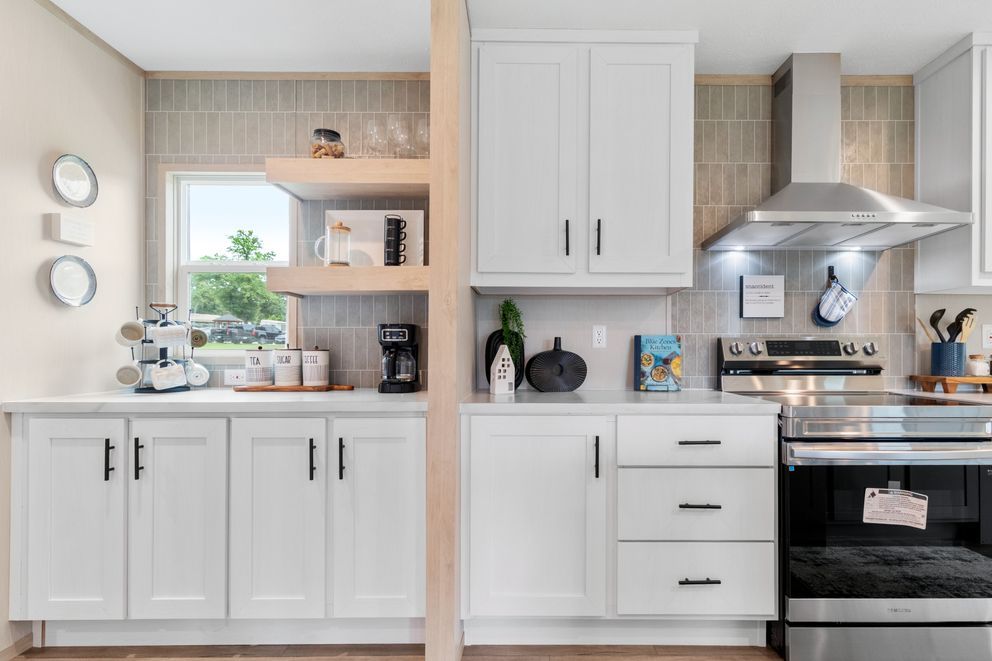 Modern white kitchen with stainless steel appliances, open shelving, and black hardware.