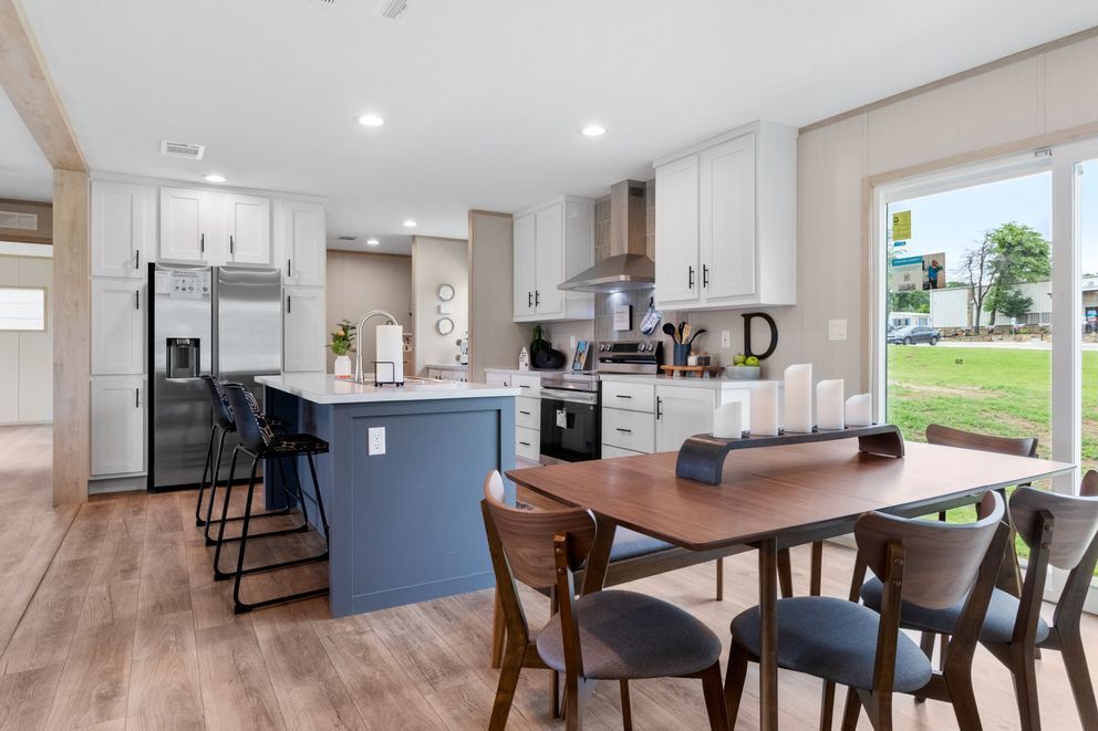 Modern kitchen and dining area with white cabinets, blue island, and wooden dining table.