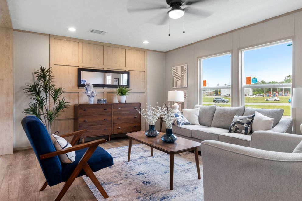 Living room with furniture, windows, and ceiling fan. Neutral colors, wooden accents, and decorative items.