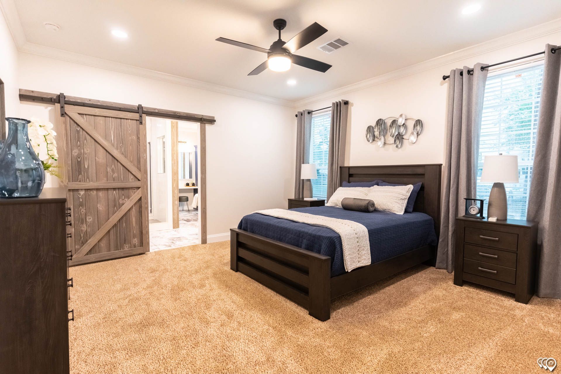 Bedroom with a bed, dresser, barn door, and ceiling fan. Brown carpet and blue/gray decor.