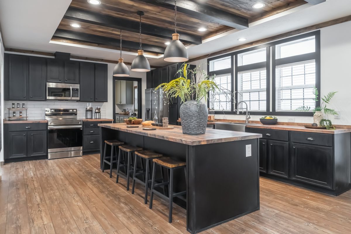 Modern kitchen with black cabinets, wooden ceiling beams, and a large island with stools.