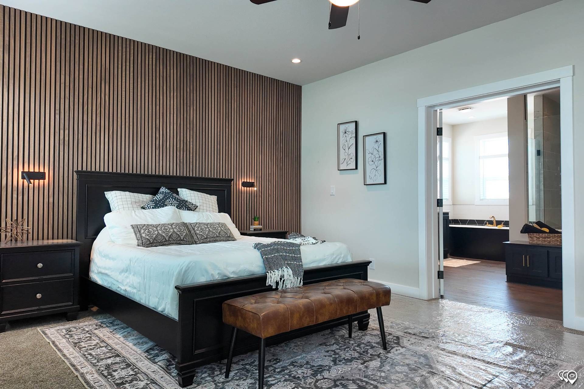 Bedroom with black bed, patterned rug, brown accent wall, and open doorway to bathroom.