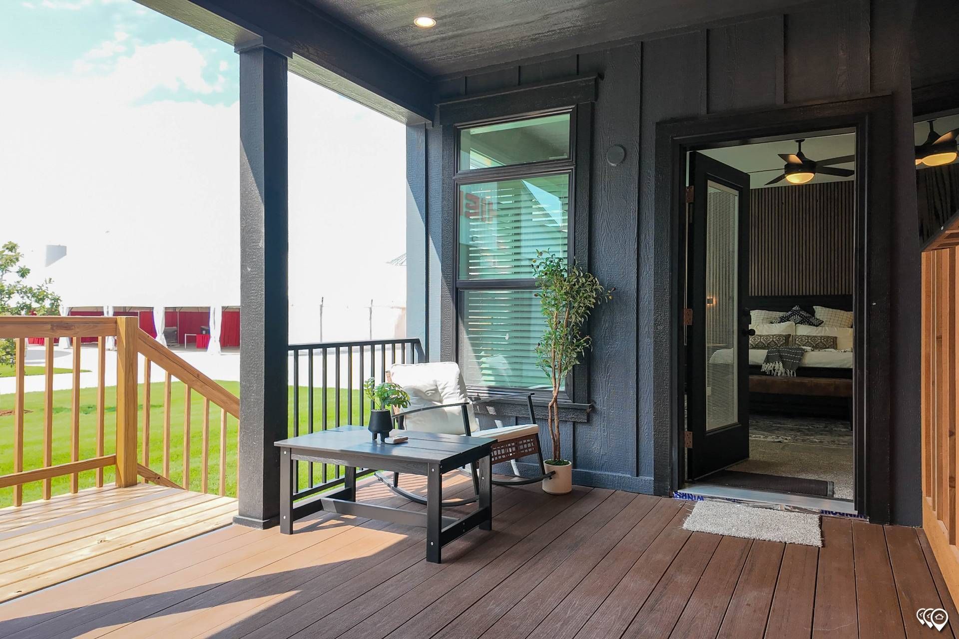 A porch with seating area and a view of a bedroom. Black and brown wood with a bright, sunny view.