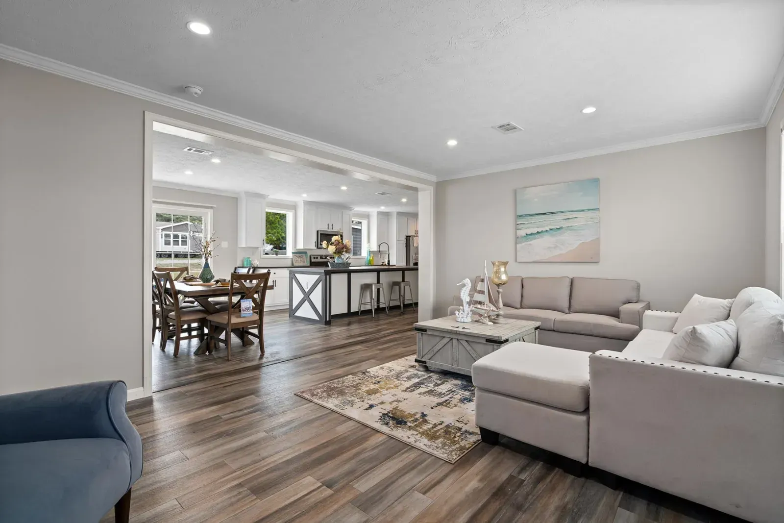 Living room with open concept to dining and kitchen, light gray walls, wooden floors, beige furniture.