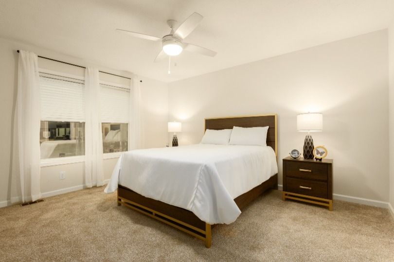 Bedroom with bed, nightstand, lamps, window, ceiling fan, and beige carpet.